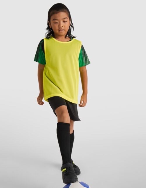Barn spiller fodbold i gul vest og sorte shorts
