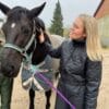 Kvinde klapper sort hest udenfor staldbygning