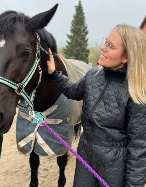 Kvinde klapper sort hest udenfor staldbygning