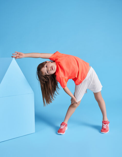 Barn strækker sig i farverigt tøj mod blå baggrund.