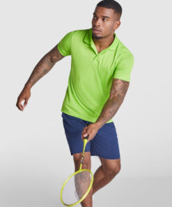 Mand spiller badminton i grøn polo og blå shorts.