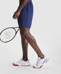 Mand spiller tennis i shorts og sneakers