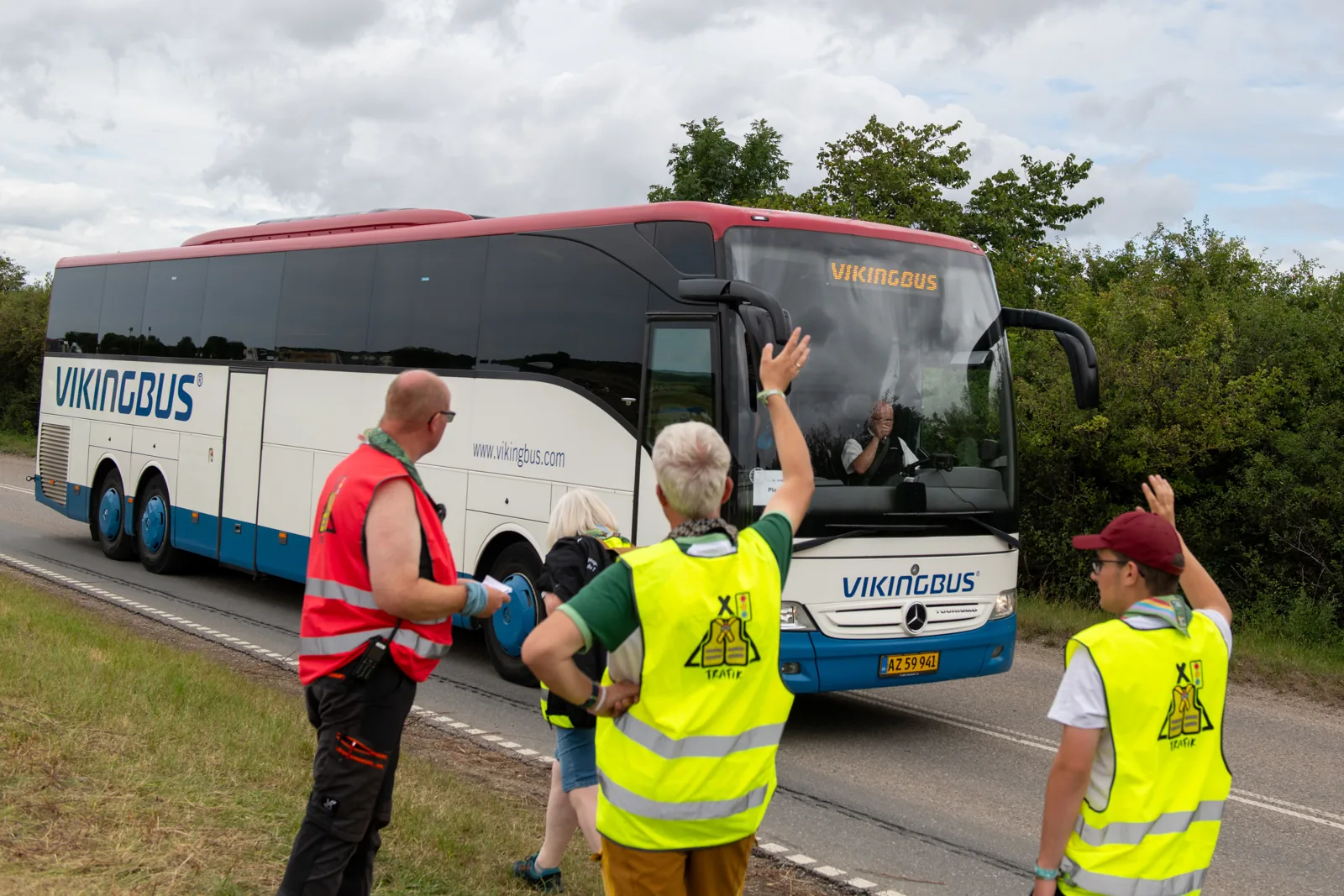 Tre frivillige i gule og røde refleksveste vinker en Vikingbus videre ved Spejdernes Lejr 2026