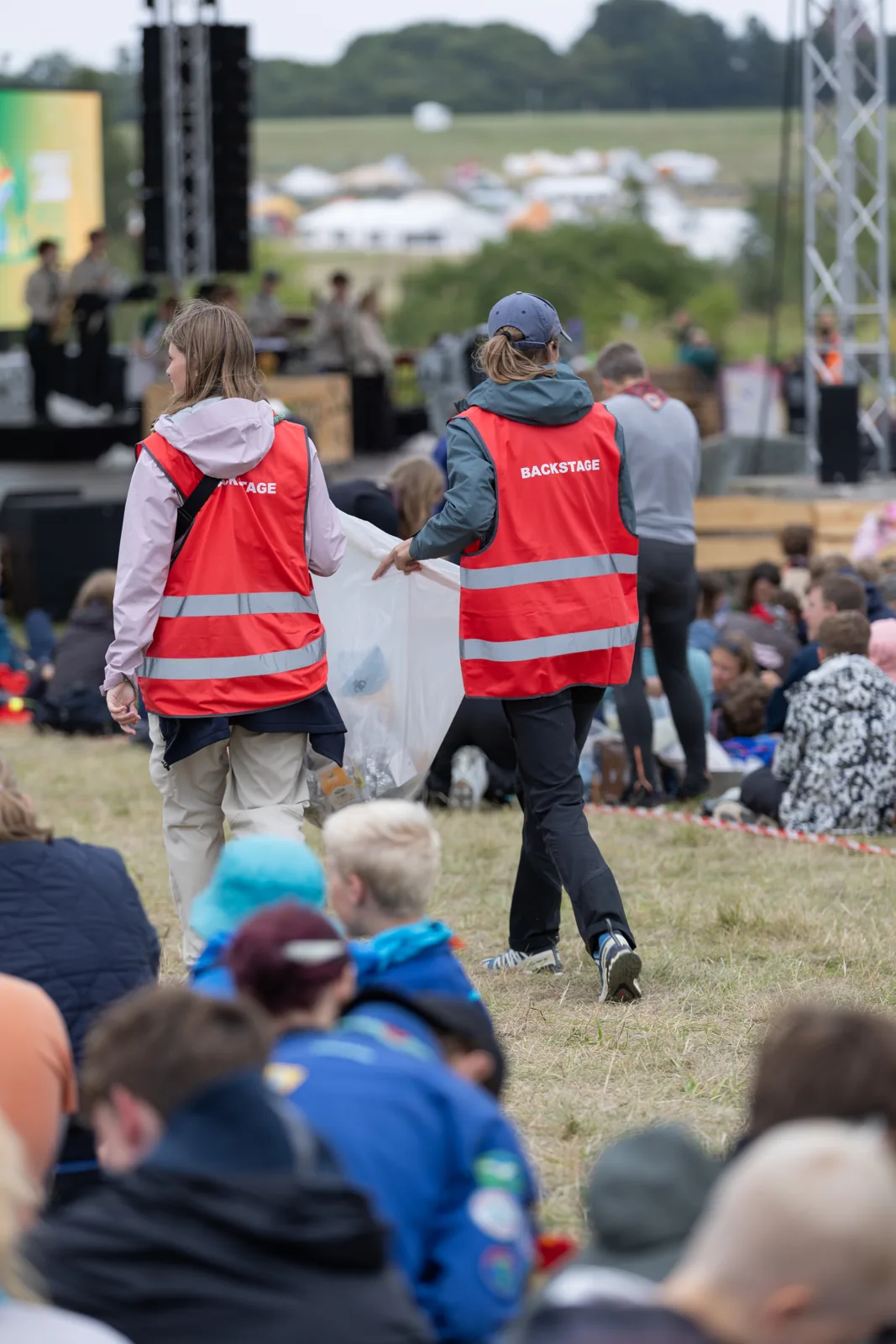 To frivillige i røde veste med backstage-tryk rydder op foran scenen på Spejdernes Lejr 2026